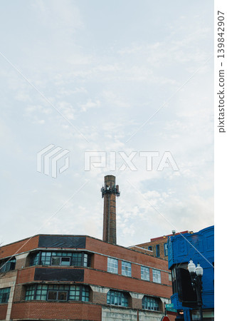 Tall chimney rises above red brick building under cloudy sky in urban area during daytime Tall chimney rises above red brick building under cloudy sky in urban area during daytime 139842907