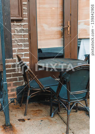 Table and chairs placed outside a building on a city street at midday with a view of the entrance and window blinds Table and chairs placed outside a building on a city street at midday with a view of the entrance and window blinds 139842908