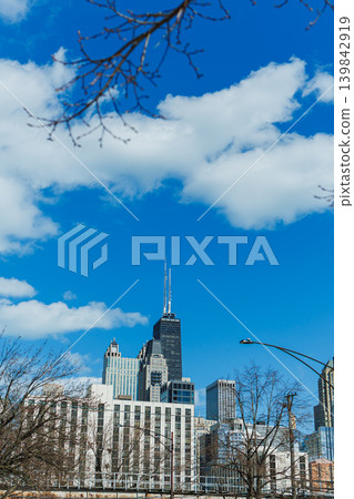 Clouds float above city buildings with a tall tower reaching into the sky during a bright day in downtown Chicago Clouds float above city buildings with a tall tower reaching into the sky during a bright day in downtown Chicago 139842919