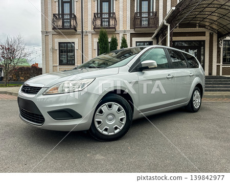 Silver car parked outside a building on a cloudy day in a quiet area with few trees and a clear path Silver car parked outside a building on a cloudy day in a quiet area with few trees and a clear path 139842977