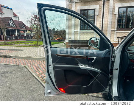 Door of a silver car open in a driveway near a house with a garden and playground on a cloudy day Door of a silver car open in a driveway near a house with a garden and playground on a cloudy day 139842982