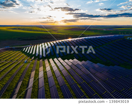 Solar panels stretch across a large field at sunset with clouds in the sky and green hills in the background Solar panels stretch across a large field at sunset with clouds in the sky and green hills in the background 139843019