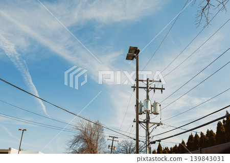 Power lines and clouds in a clear sky above a street in a suburban area during the day in early spring 139843031