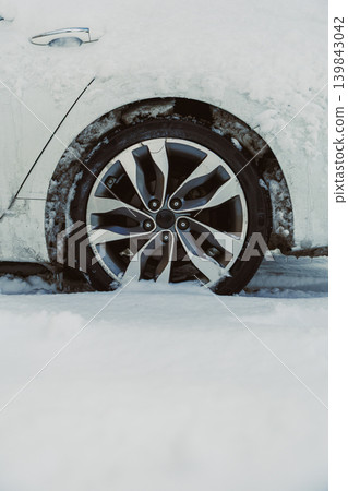 Winter scene shows a car wheel stuck in deep snow in a cold landscape during a snowfall 139843042