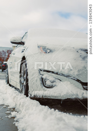 Snow covers a parked car in a city parking lot during winter on a cloudy day Snow covers a parked car in a city parking lot during winter on a cloudy day 139843043