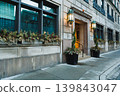 Entrance of a building with large windows and plants on a city sidewalk during the evening 139843047