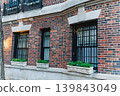 Windows of a brick building in a city with green plants in pots under each window during early evening light 139843049