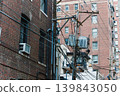 City alley shows brick buildings and utility poles with wires during a cloudy day in an urban setting 139843050