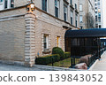 Corner of a building with a light fixture at night in an urban setting with a sidewalk and plants in view 139843052