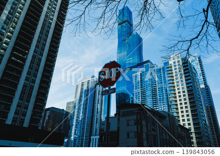 Tall buildings rise against the sky with a stop sign visible in the foreground during daylight in an urban city setting Tall buildings rise against the sky with a stop sign visible in the foreground during daylight in an urban city setting 139843056