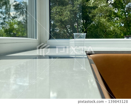Luminous table adjacent to window showcasing cold drink against vibrant greenery and elegant surroundings Luminous table adjacent to window showcasing cold drink against vibrant greenery and elegant surroundings 139843128