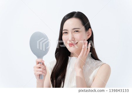 A woman checks her skin in a hand mirror. A woman checks her skin in a hand mirror. 139843133