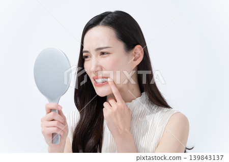 A woman checks her skin in a hand mirror. 139843137