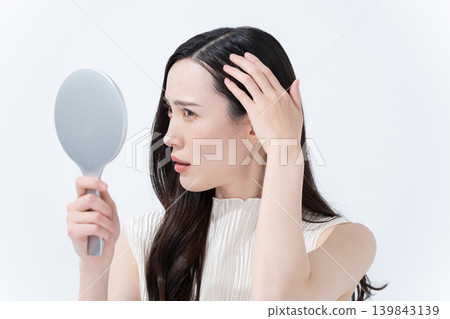 A woman checks her hairline in a hand mirror. A woman checks her hairline in a hand mirror. 139843139