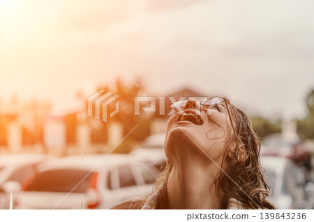Woman rain joy catching raindrops in her mouth with head tilted back enjoying freedom during summer storm in city street Woman rain joy catching raindrops in her mouth with head tilted back enjoying freedom during summer storm in city street 139843236