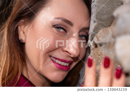 Woman smiling wall happy adult woman leaning her face against a textured stone surface with a confident expression Woman smiling wall happy adult woman leaning her face against a textured stone surface with a confident expression 139843239