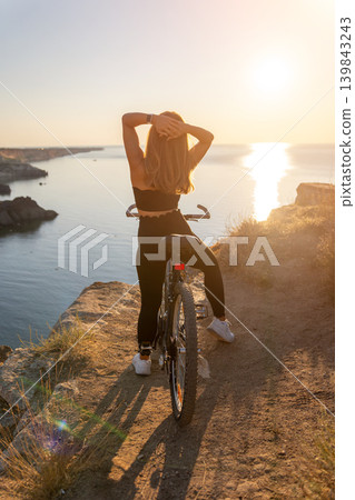 Woman sunset bicycle woman sitting on a bicycle at a cliff edge watching the sunset over the sea in a peaceful moment Woman sunset bicycle woman sitting on a bicycle at a cliff edge watching the sunset over the sea in a peaceful moment 139843243