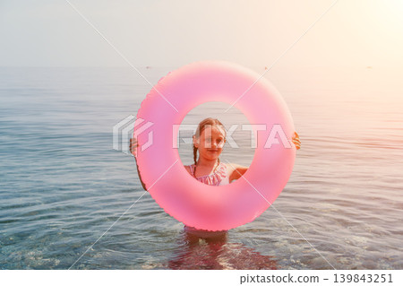 Child ocean vacation young girl standing in sea water holding large pink inflatable ring during golden hour summer holidays 139843251