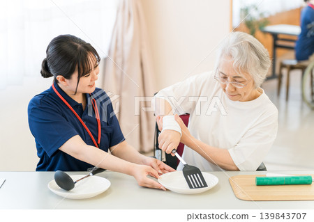 職能治療師和女性護理經理使用烹飪用具幫助老年女性進行復健。 職能治療師和女性護理經理使用烹飪用具幫助老年女性進行復健。 139843707