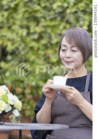 一位老婦人在自家院子裡一邊喝咖啡一邊種花。 一位老婦人在自家院子裡一邊喝咖啡一邊種花。 139844191