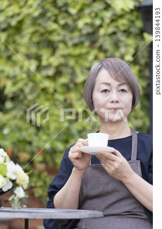 A senior woman drinking coffee while gardening in her yard. A senior woman drinking coffee while gardening in her yard. 139844193