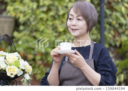 A senior woman drinking coffee while gardening in her yard. 139844194