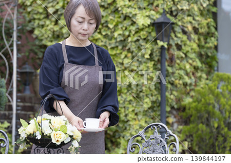 一位老婦人在自家院子裡一邊喝咖啡一邊種花。 一位老婦人在自家院子裡一邊喝咖啡一邊種花。 139844197