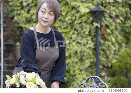 一位老婦人在自家院子裡一邊喝咖啡一邊種花。 一位老婦人在自家院子裡一邊喝咖啡一邊種花。 139844201