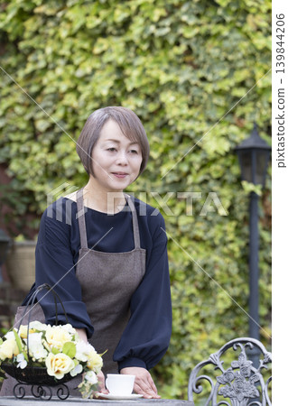 一位老婦人在自家院子裡一邊喝咖啡一邊種花。 一位老婦人在自家院子裡一邊喝咖啡一邊種花。 139844206