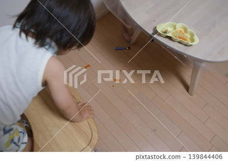 The back view of a child peering at food spills on the floor. 139844406