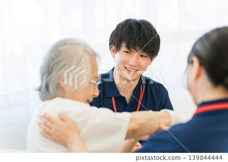 Senior woman undergoing rehabilitation and caregiver, male and female occupational therapist staff 139844444
