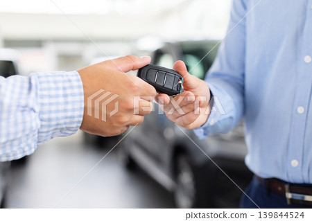 Customer receiving car keys from professional salesman after successful automobile purchase Customer receiving car keys from professional salesman after successful automobile purchase 139844524