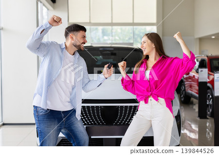 Excited young couple celebrating new car purchase at dealership showroom Excited young couple celebrating new car purchase at dealership showroom 139844526