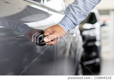 Customer opening new vehicle door with keyless handle system inside car dealership 139844528