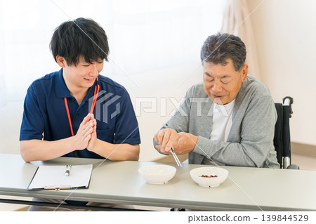 Male patient and caregiver doing bean-grabbing training at a nursing home, hospital, or rehabilitation center Male patient and caregiver doing bean-grabbing training at a nursing home, hospital, or rehabilitation center 139844529