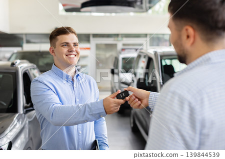 Friendly car salesman handing vehicle keys to customer after successful automobile purchase Friendly car salesman handing vehicle keys to customer after successful automobile purchase 139844539