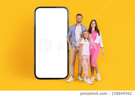 Smiling caucasian family standing beside oversized smartphone mockup on yellow studio background Smiling caucasian family standing beside oversized smartphone mockup on yellow studio background 139844562