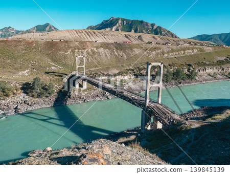 A weathered suspension bridge stretches over the brilliant turquoise waters of the Katun River in the scenic Altai region A weathered suspension bridge stretches over the brilliant turquoise waters of the Katun River in the scenic Altai region 139845139