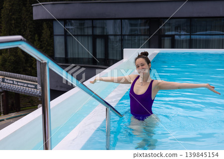Happy woman relaxing in outdoor swimming pool with arms open. Wellness travel lifestyle, spa resort vacation, healthy leisure activity, aqua fitness. 139845154