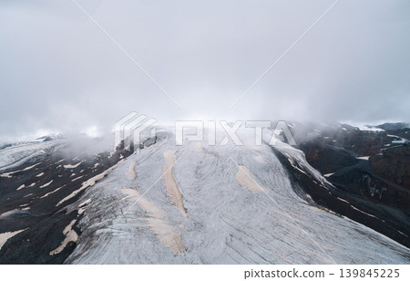 Aerial view of cracked epic glacier Elbrus Caucasus mountain. Snow-capped highest peaks in fog clouds, glacier melting. Aerial view of cracked epic glacier Elbrus Caucasus mountain. Snow-capped highest peaks in fog clouds, glacier melting. 139845225