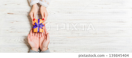 Top view of a gift in male and female hands on wooden background. Congratulation of each other concept. Copy space Top view of a gift in male and female hands on wooden background. Congratulation of each other concept. Copy space 139845404