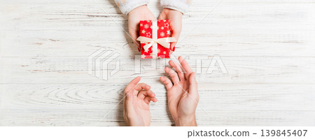 Top view of holding a gift in female and male hands on wooden background. Woman and man give and receive a present. Close up of time for holiday concept Top view of holding a gift in female and male hands on wooden background. Woman and man give and receive a present. Close up of time for holiday concept 139845407