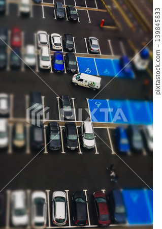 High angle tilt-shift view of a city parking lot with blue accessible spaces. Concept of smart urban planning, logistics, and infrastructure management. Miniature world aesthetic for tech brands. High angle tilt-shift view of a city parking lot with blue accessible spaces. Concept of smart urban planning, logistics, and infrastructure management. Miniature world aesthetic for tech brands. 139845833