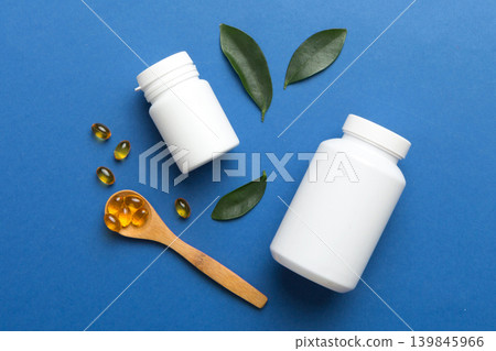 Omega-3 capsules lie in white bottle on a table with green leaves background. Fish oil tablets. Biologically active additives. omega 6, omega 9, vitamin A, E, D, vitamin D3 top view with copy space Omega-3 capsules lie in white bottle on a table with green leaves background. Fish oil tablets. Biologically active additives. omega 6, omega 9, vitamin A, E, D, vitamin D3 top view with copy space 139845966