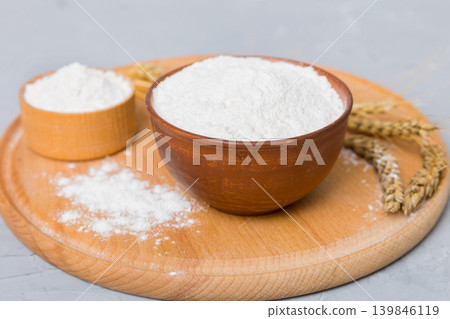 Flat lay of Wheat flour in wooden bowl with wheat spikelets on colored background. world wheat crisis Flat lay of Wheat flour in wooden bowl with wheat spikelets on colored background. world wheat crisis 139846119