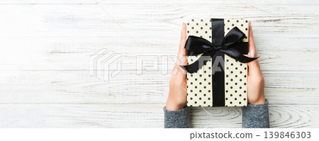 Top view of female hands holding christmas or other holiday handmade present box package in the palms, flat lay on white rustic table background with copy space Top view of female hands holding christmas or other holiday handmade present box package in the palms, flat lay on white rustic table background with copy space 139846303