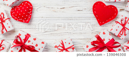 Valentine or other holiday handmade present in paper with red hearts and gifts box in holiday wrapper. Present box of gift on white wooden table top view with copy space, empty space for design Valentine or other holiday handmade present in paper with red hearts and gifts box in holiday wrapper. Present box of gift on white wooden table top view with copy space, empty space for design 139846308