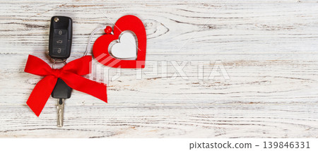 Car key with a red ribbon adn a heart on white wooden table. Giving present or gift for valentine's day or christmas Car key with a red ribbon adn a heart on white wooden table. Giving present or gift for valentine's day or christmas 139846331