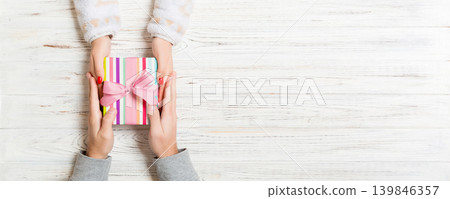 Top view of two people sharing a present on wooden background. Holiday and surprise concept. Copy space Top view of two people sharing a present on wooden background. Holiday and surprise concept. Copy space 139846357