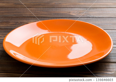 Perspective view of empty orange plate on wooden background. Empty space for your design Perspective view of empty orange plate on wooden background. Empty space for your design 139846603